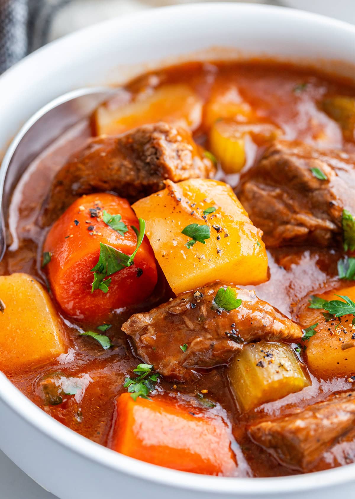 A bowl of crockpot beef stew with beef pieces, potatoes, and carrots, topped with fresh parsley.