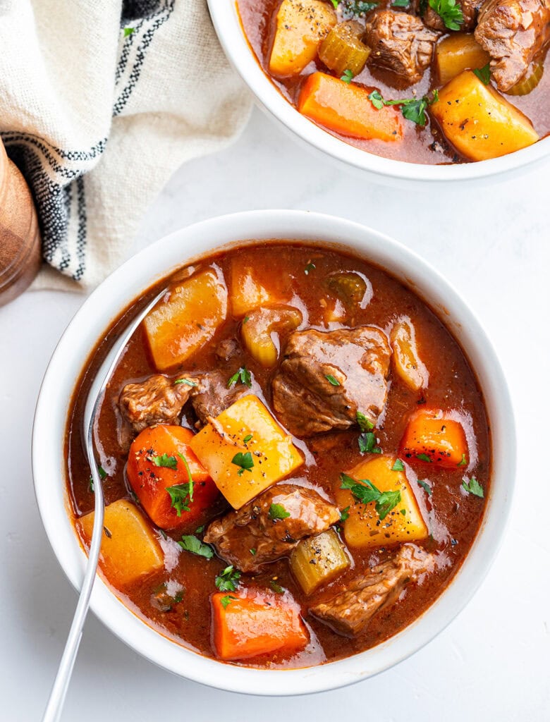 A bowl of crockpot beef stew with beef pieces, potatoes, and carrots, topped with fresh parsley.