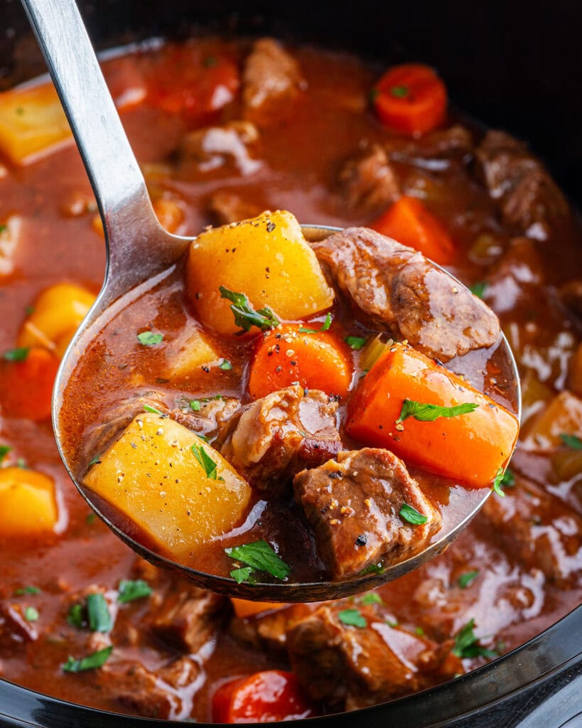 A ladle of beef stew with pieces of potatoes, and carrots.