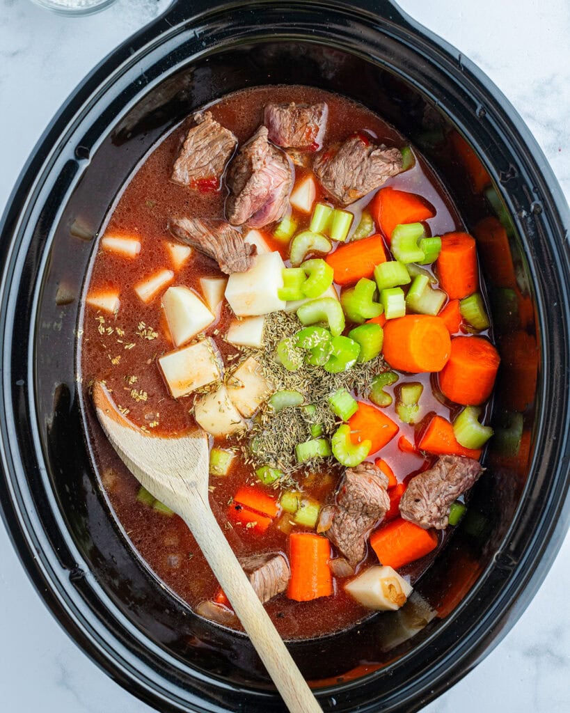 The ingredients needed to make beef stew all mixed in a crockpot, uncooked.