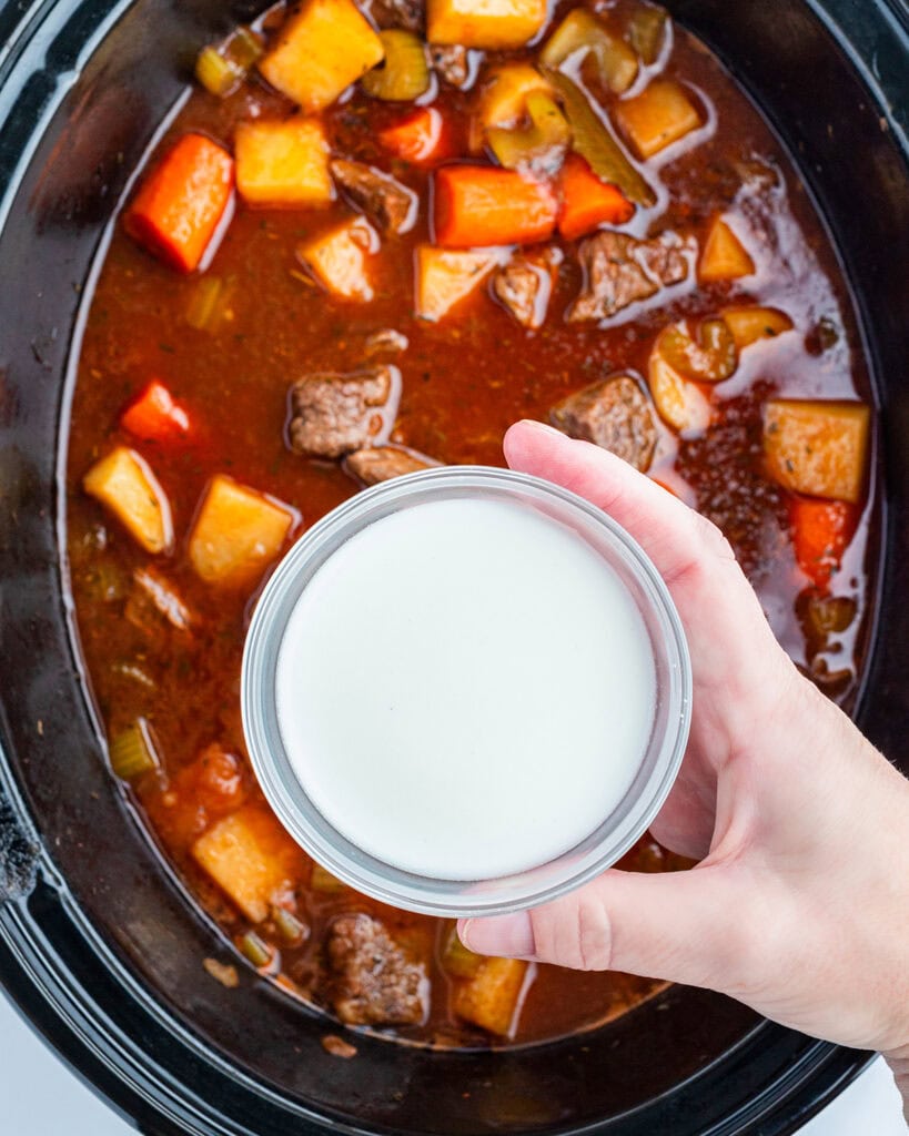 A slurry of cornstarch and water in a small bowl above a crockpot of beef stew.