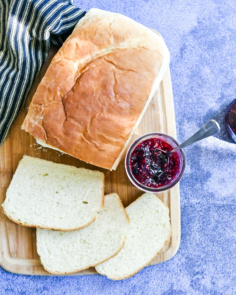 Raspberry blueberry jam in a jar alongside sliced bread 