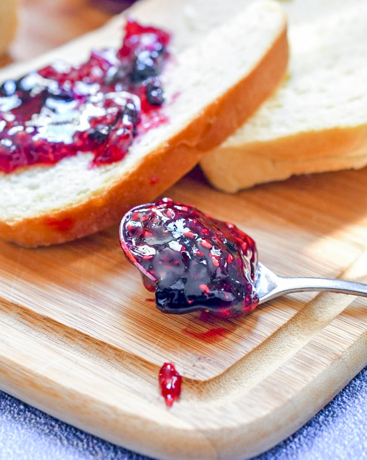 A spoonful of raspberry blueberry jam on a cutting board with jam on a slice of bread behind