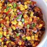 A close up of a bowl of southwest salsa with corn, blackbeans, tomatoes, and cilantro.