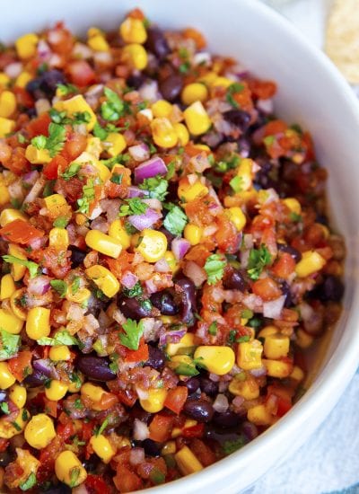 A close up of a bowl of southwest salsa with corn, blackbeans, tomatoes, and cilantro.