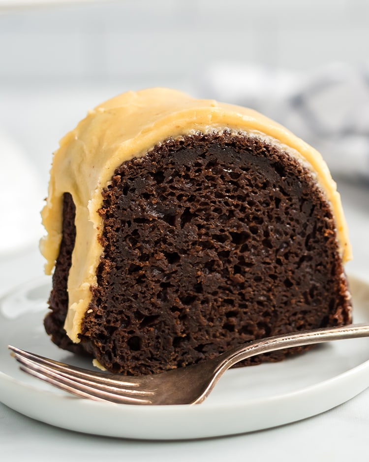 A slice of Chocolate Pumpkin Bundt Cake topped with a pumpkin icing on a plate. 