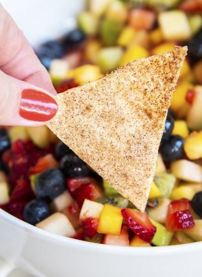 A hand holding a chip covered in cinnamon sugar.