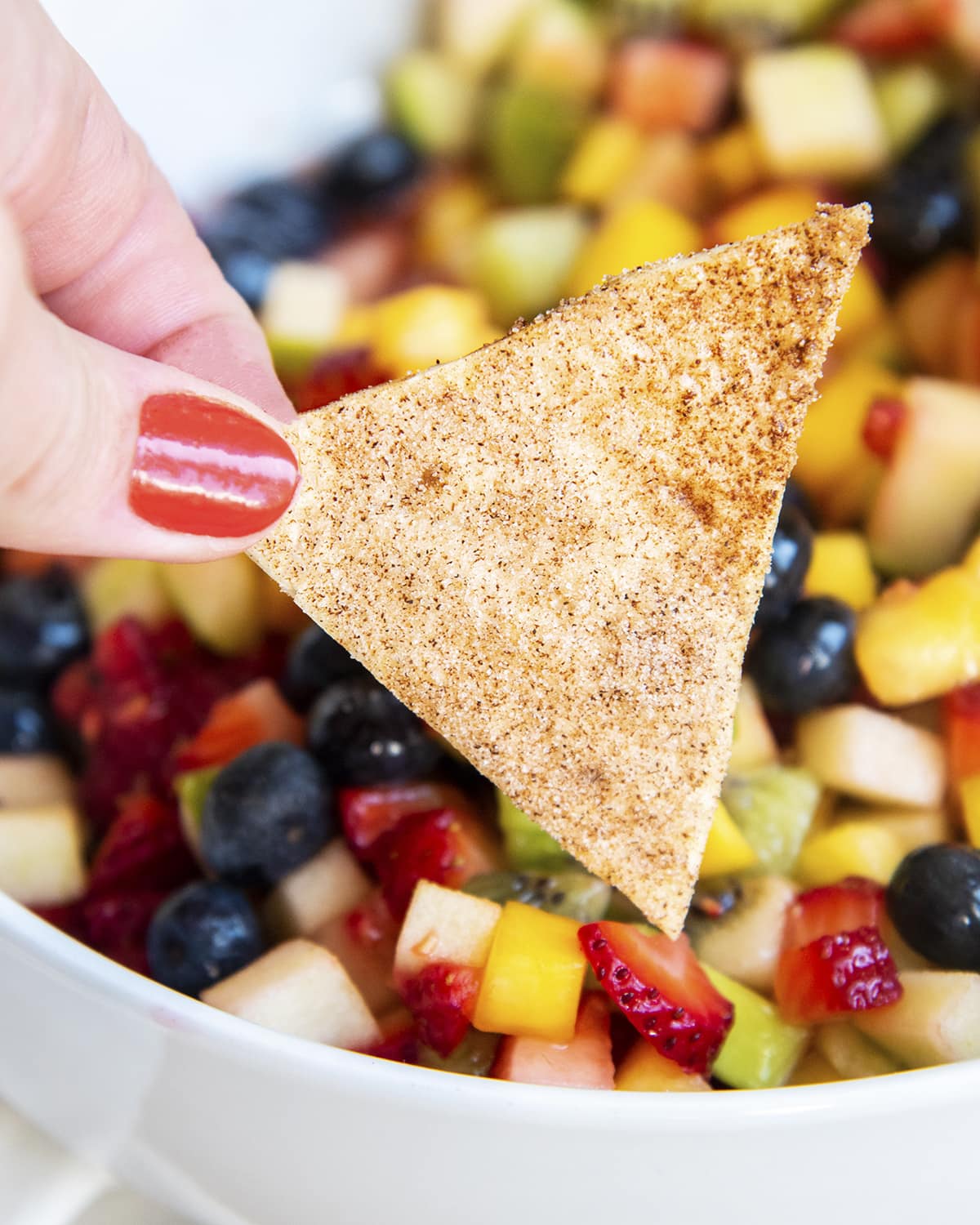 A hand holding a chip covered in cinnamon sugar.