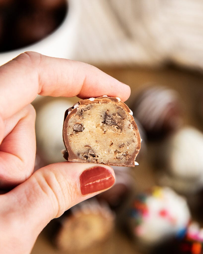 A hand holding half of a cookie dough ball full of chocolate chips.