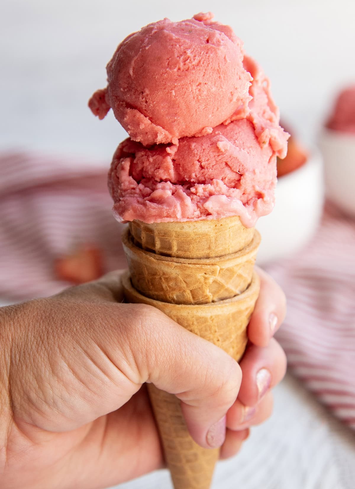 A hand holding an ice cream cone with strawberry sherbet in it.