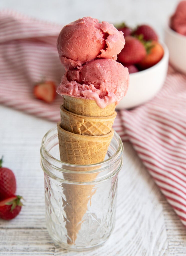 An ice cream cone topped with a pink ice cream, sitting in a jar.