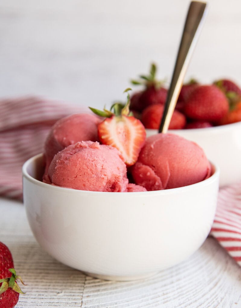 A bowl of pink strawberry sherbet topped with a fresh strawberry.