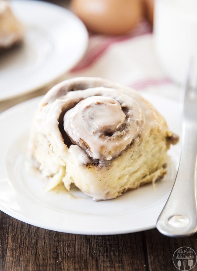 A cinnamon roll on a plate with an icing on top. 