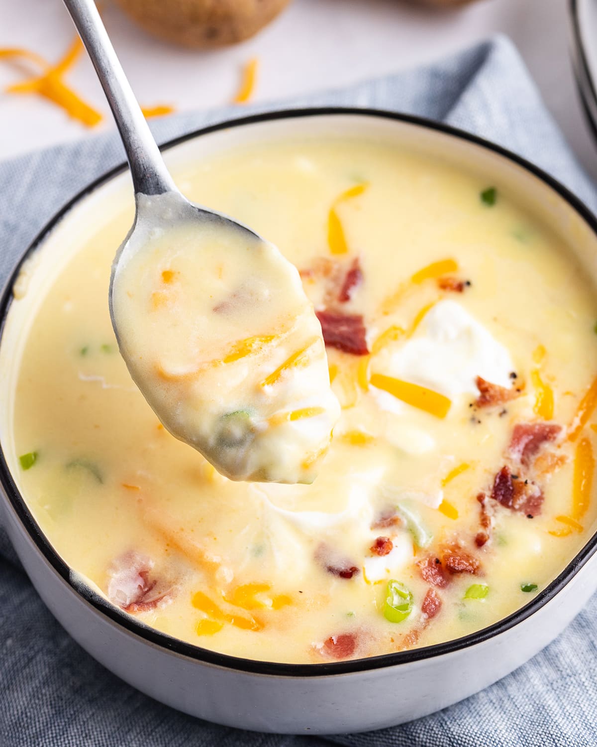 A spoonful of baked potato soup above the bowl of soup. 