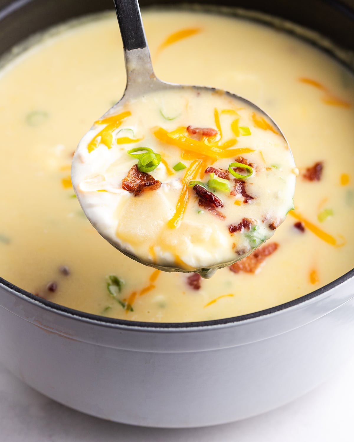 A ladle of baked potato soup above a pot of it.