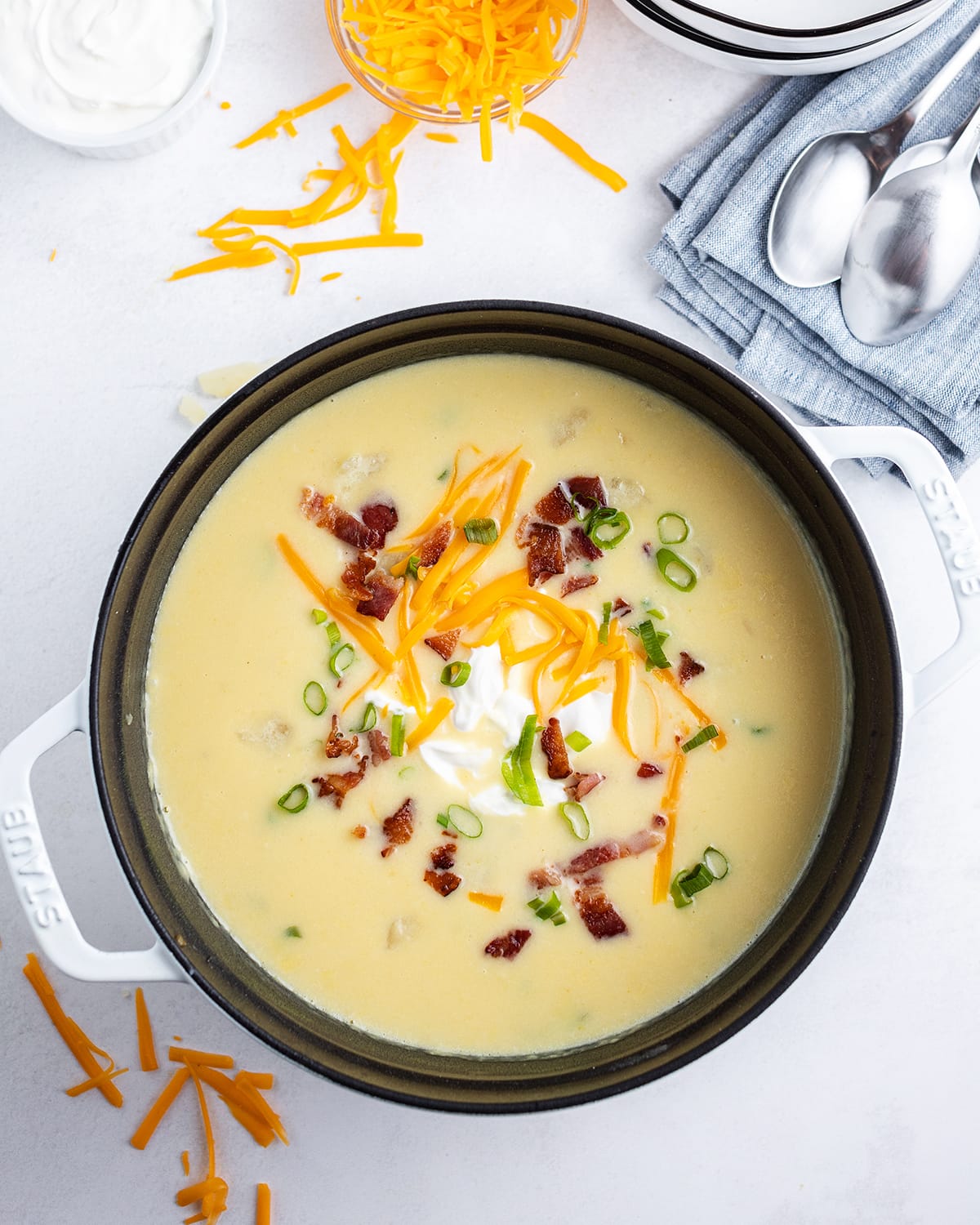 A pot of baked potato soup topped with sour cream, shredded cheese, crumbled bacon, and green onion.