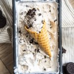 Cookies and cream ice cream in a cone on top of more ice cream in a pan