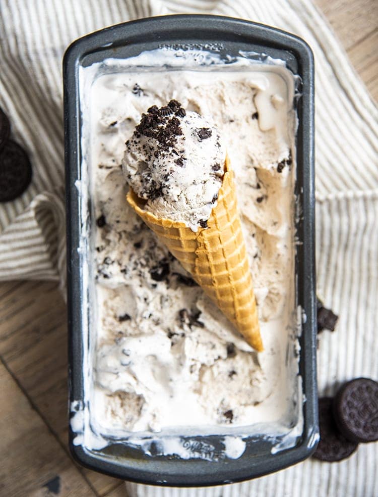 Cookies and cream ice cream in a cone on top of more ice cream in a pan