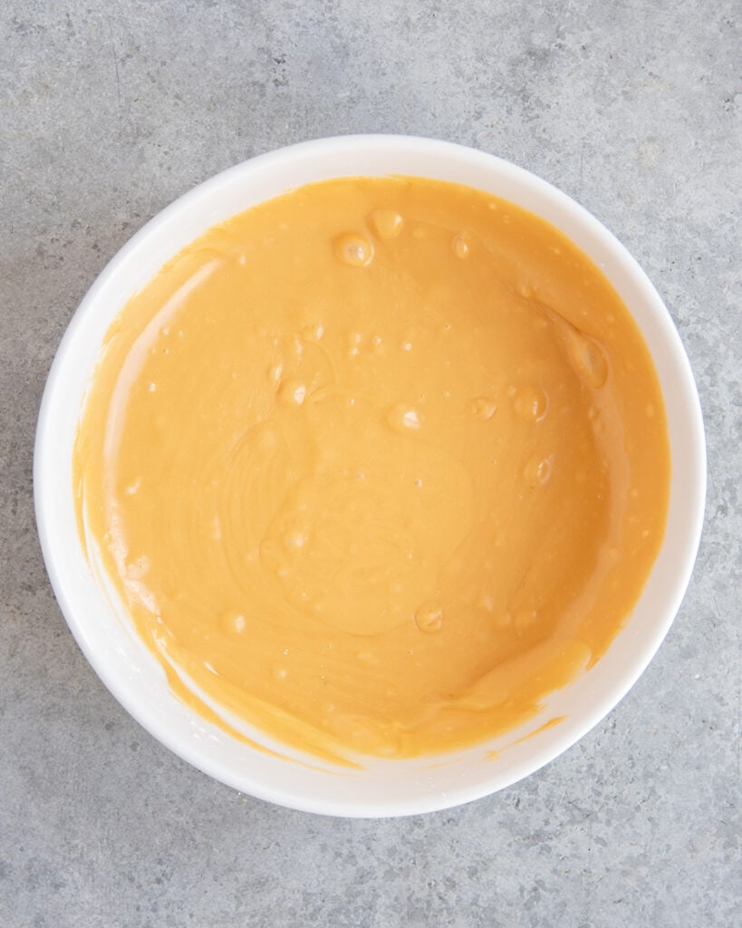 A white bowl of a melted butterscotch glaze with an orange color.