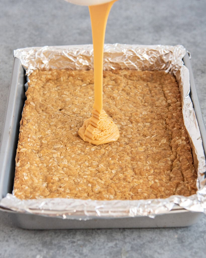 An orange glaze being poured on a pan of butterscotch bars.