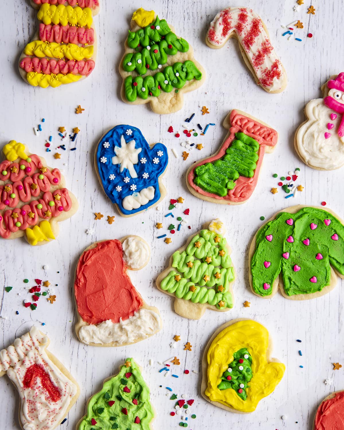 An overhead photo of several different decorated and frosted sugar cookies, Christmas trees, mittens, candy canes, and stockings.