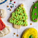 An overhead photo of a Christmas tree shaped sugar cookie surrounded by other frosted sugar cookies.