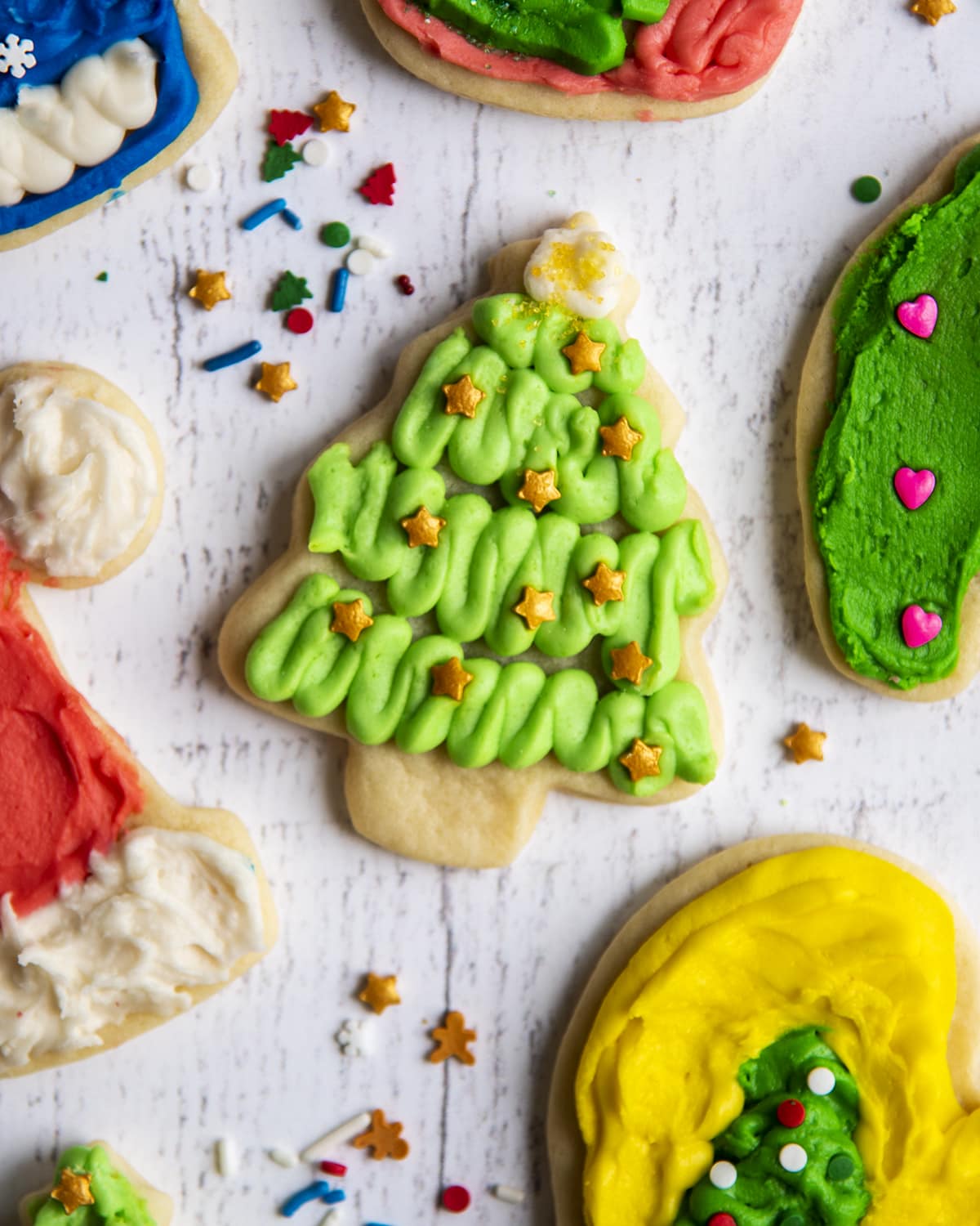 An overhead photo of a Christmas tree shaped sugar cookie surrounded by other frosted sugar cookies.