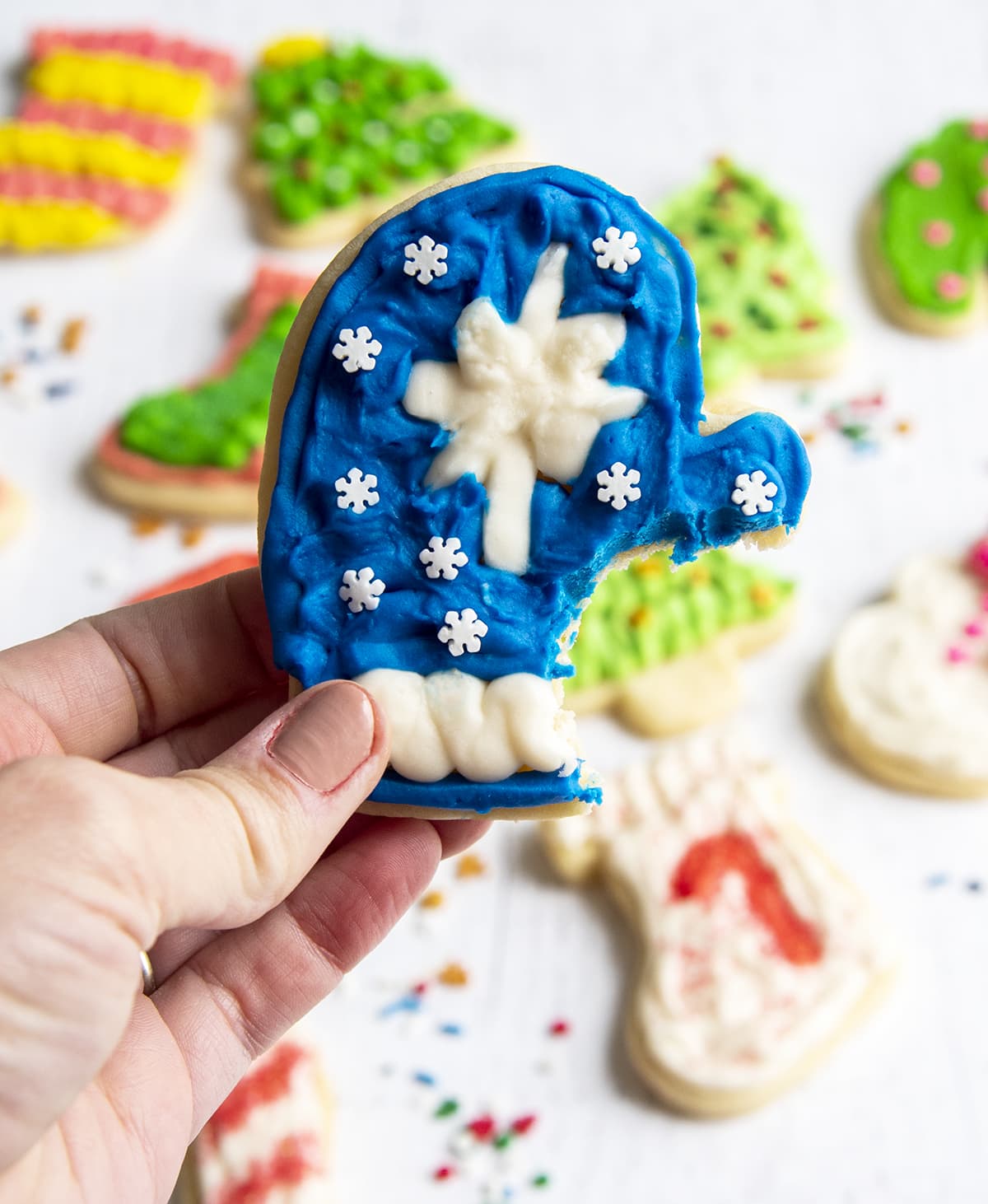 A blue frosted mitten sugar cookie with a bite out of it being held in a hand.