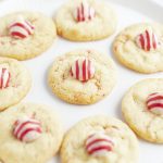 A plate of peppermint kiss cookies, each topped with a red and white striped candy Kiss.