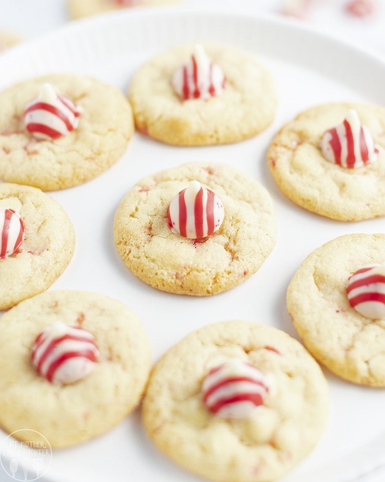 A large white plate topped with light colored cookies each topped with a red and white striped Kiss candy.