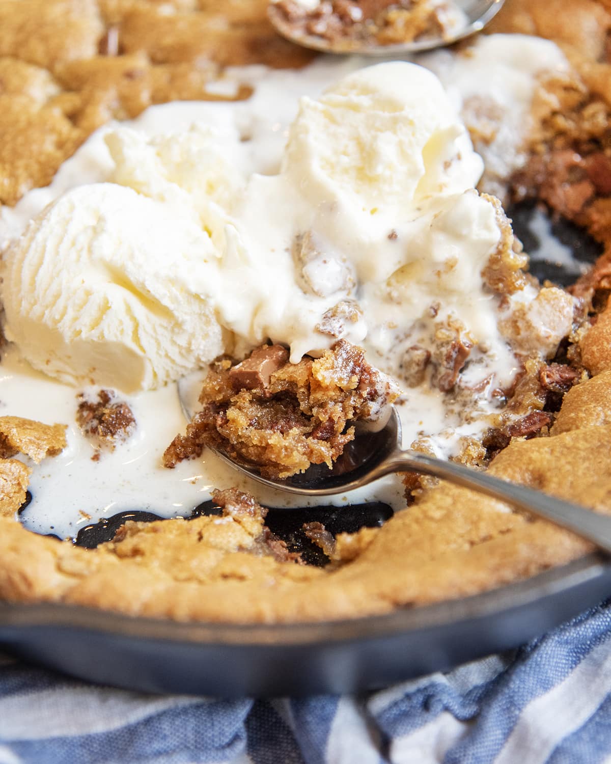 A close up of a spoonful of pizookie next to scoops of ice cream on the giant cookie. 