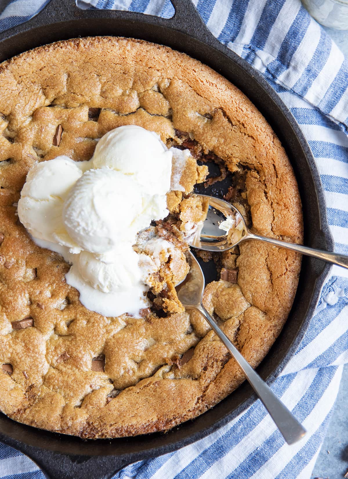 An overhead photo of a skillet full of a chocolate chunk pizookie with two spoonfuls of cookie, and ice cream.