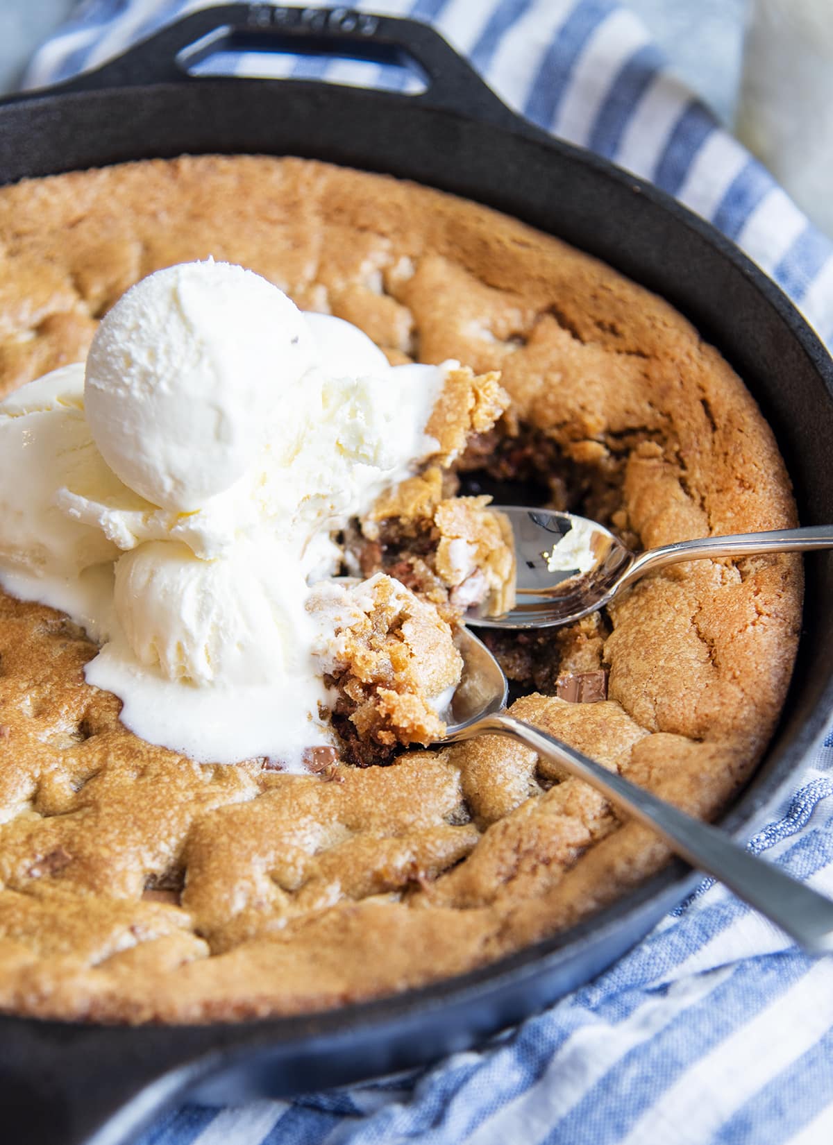 A giant skillet cookie topped with ice cream, with two spoonfuls of the dessert. 