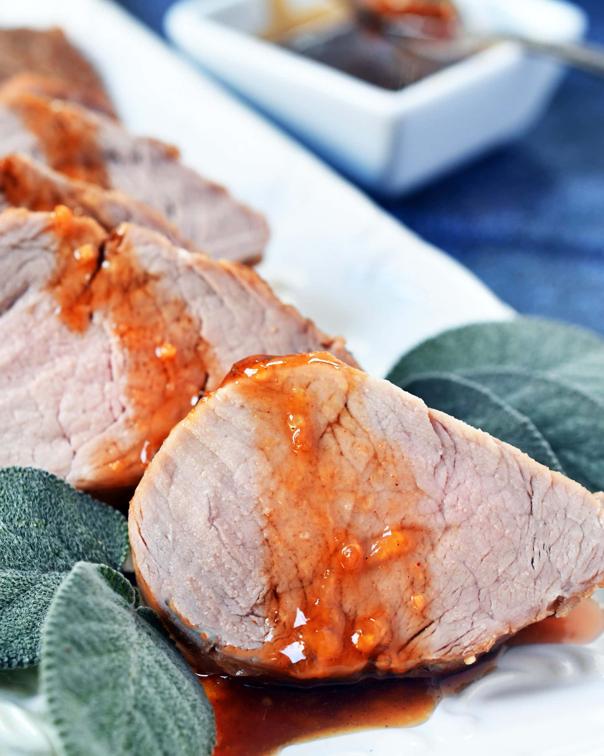 slices of pork tenderloin drizzled with peach honey sauce framed with sage leaves on a white serving dish