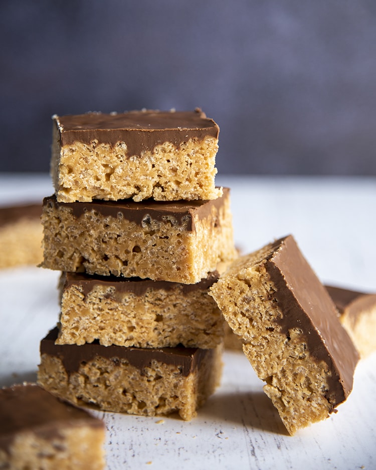 Scotcheroos stacked on top of each other with chocolate on top and one leaning on its side.