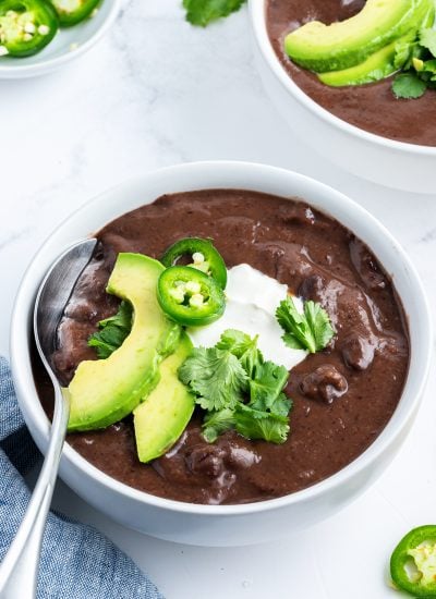 A bowl of creamy black bean soup topped with avocado slices, jalapenos, and sour cream.