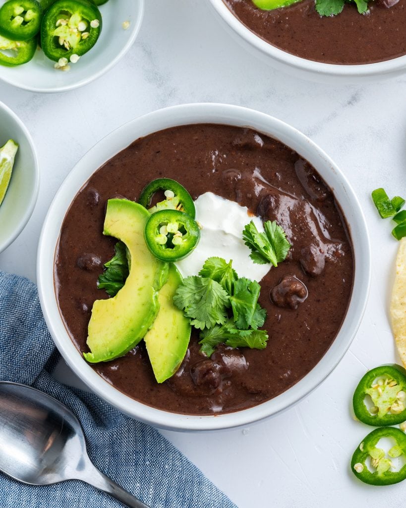 An above photo of a bowl of black bean soup with avocado, jalapeno, and cilantro on top.