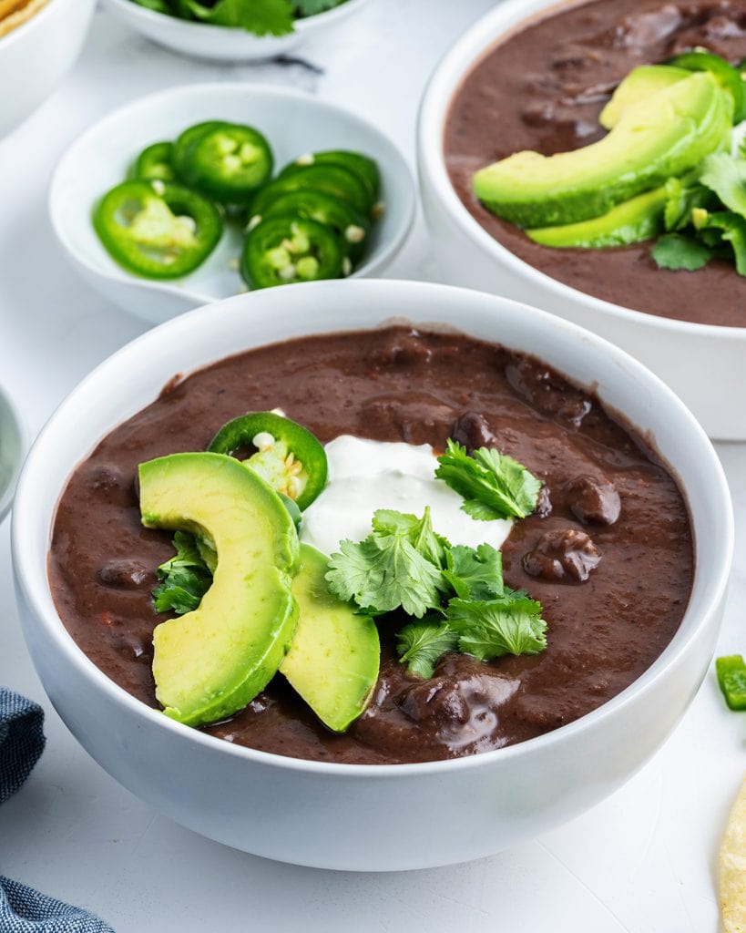 A bowl of black bean soup topped with avocado slices, and a dollop of sour cream.