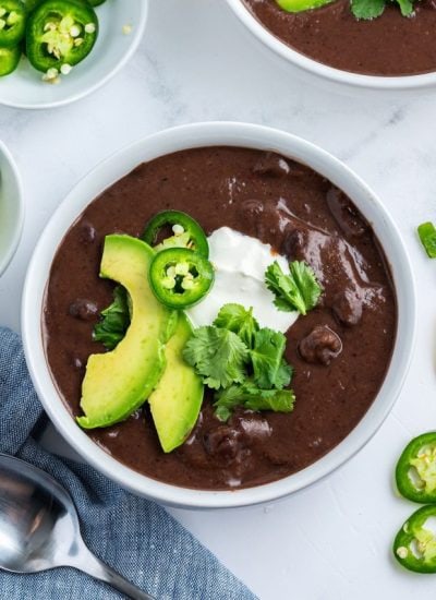 An above photo of a bowl of black bean soup with avocado, jalapeno, and cilantro on top.