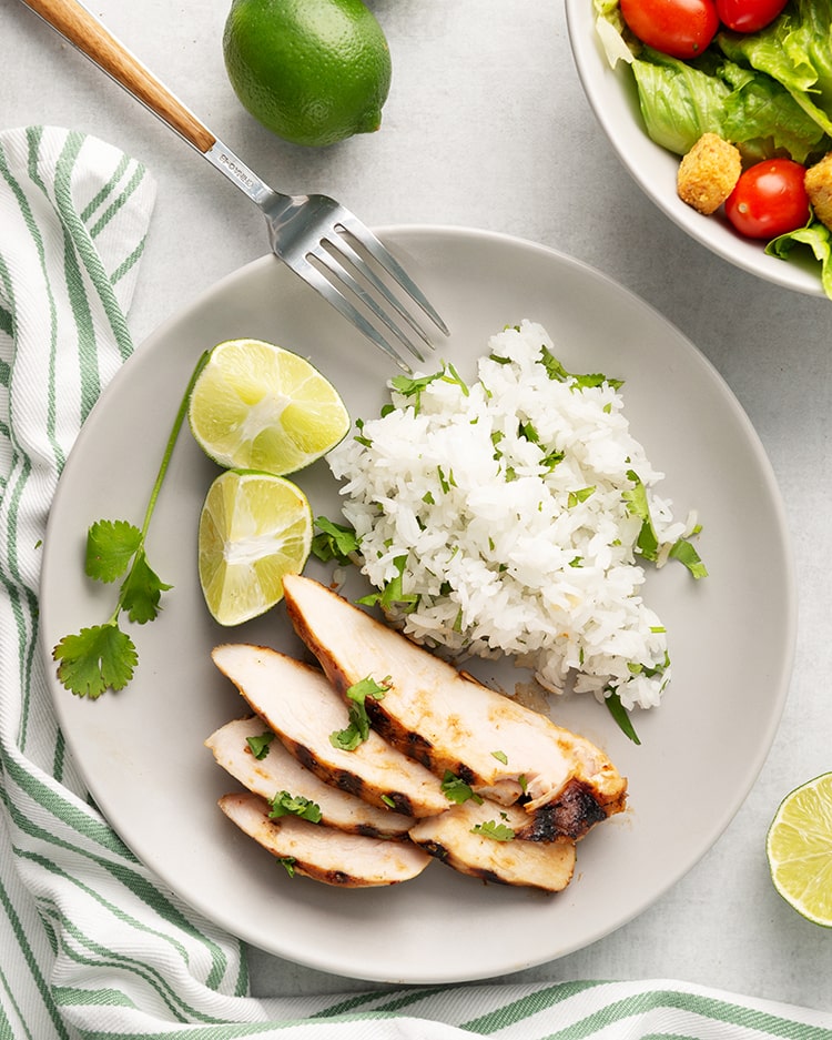 Sliced honey lime chicken on a plate with cilantro rice and limes