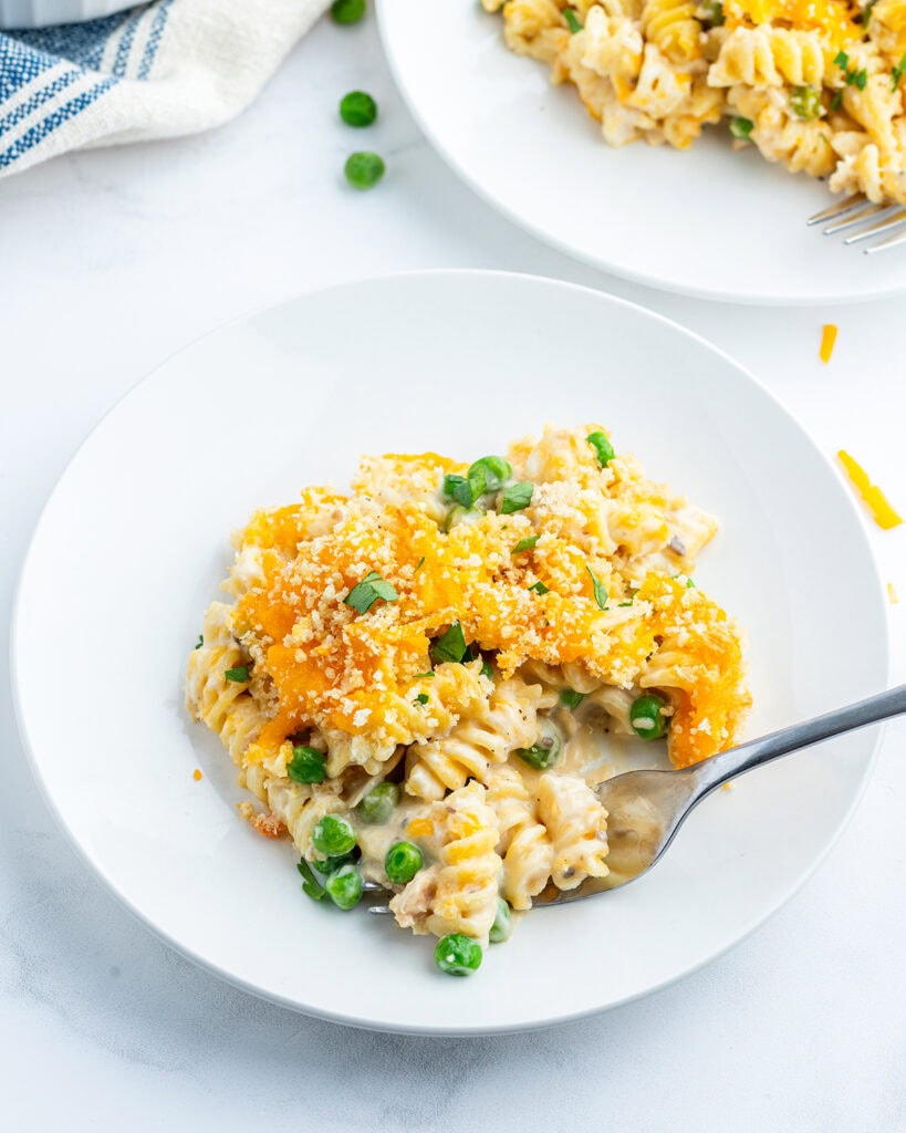 A plate of tuna casserole that is full of rotini pasta topped with melted cheese and bread crumbs.