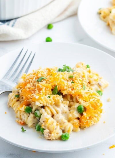 A plate of tuna casserole that is full of rotini pasta topped with melted cheese and bread crumbs.