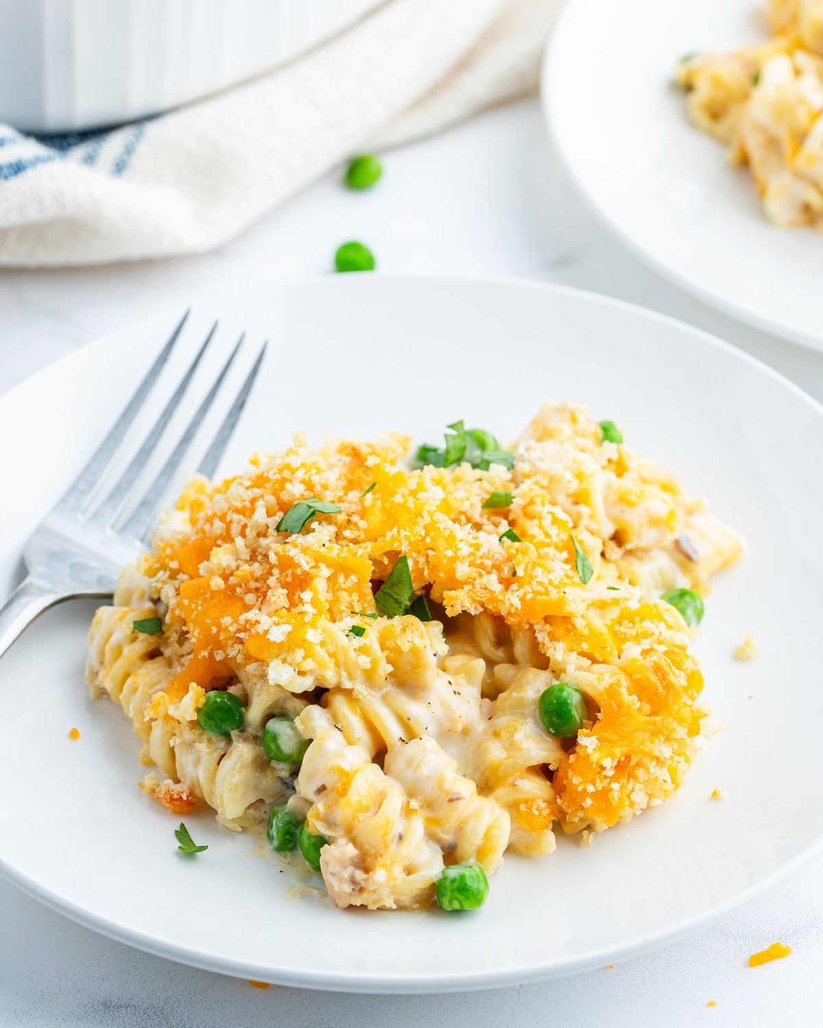 A plate of tuna casserole that is full of rotini pasta topped with melted cheese and bread crumbs.
