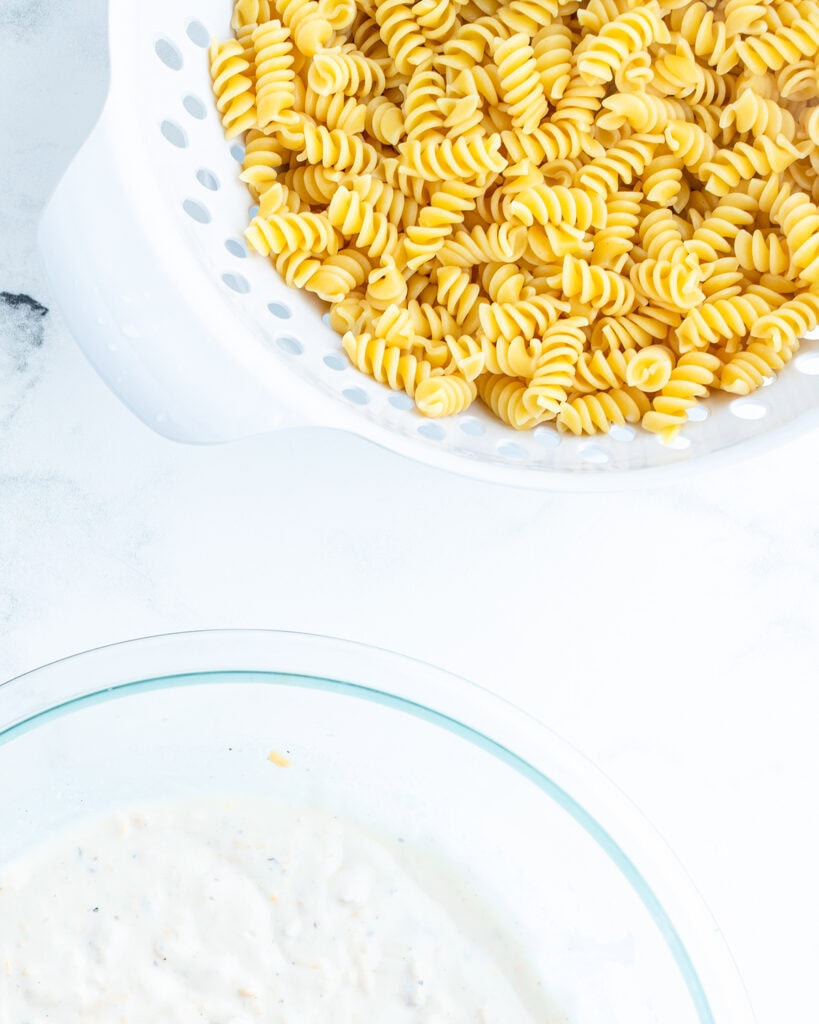A bowl of cooked pasta, and another bowl of creamy sauce.