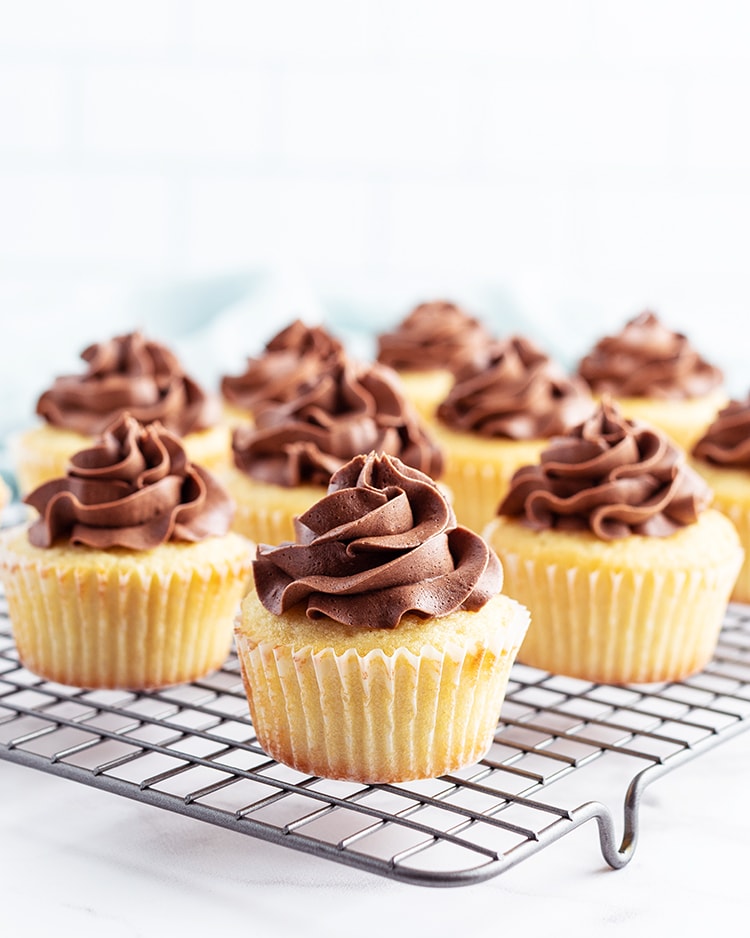 Yellow cupcakes with chocolate frosting on a cooling rack.