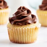 A close up of a yellow cupcake in a cupcake liner with a swirl of chocolate butter cream frosting on top.