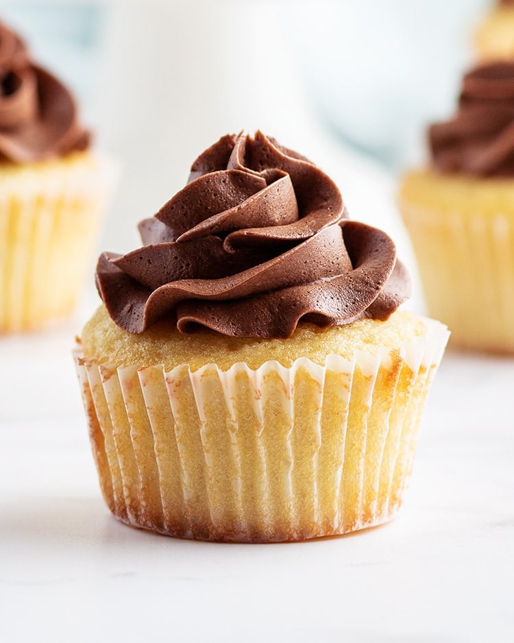 A close up of a yellow cupcake in a cupcake liner with a swirl of chocolate butter cream frosting on top.