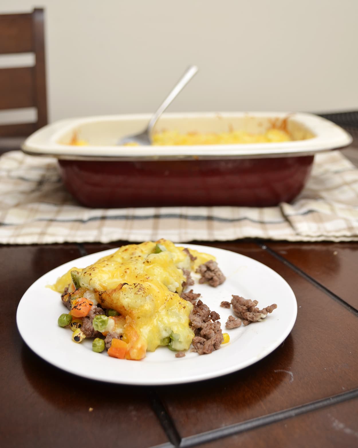 Front view of shepherds pie on a white plate with a casserole dish in the background.