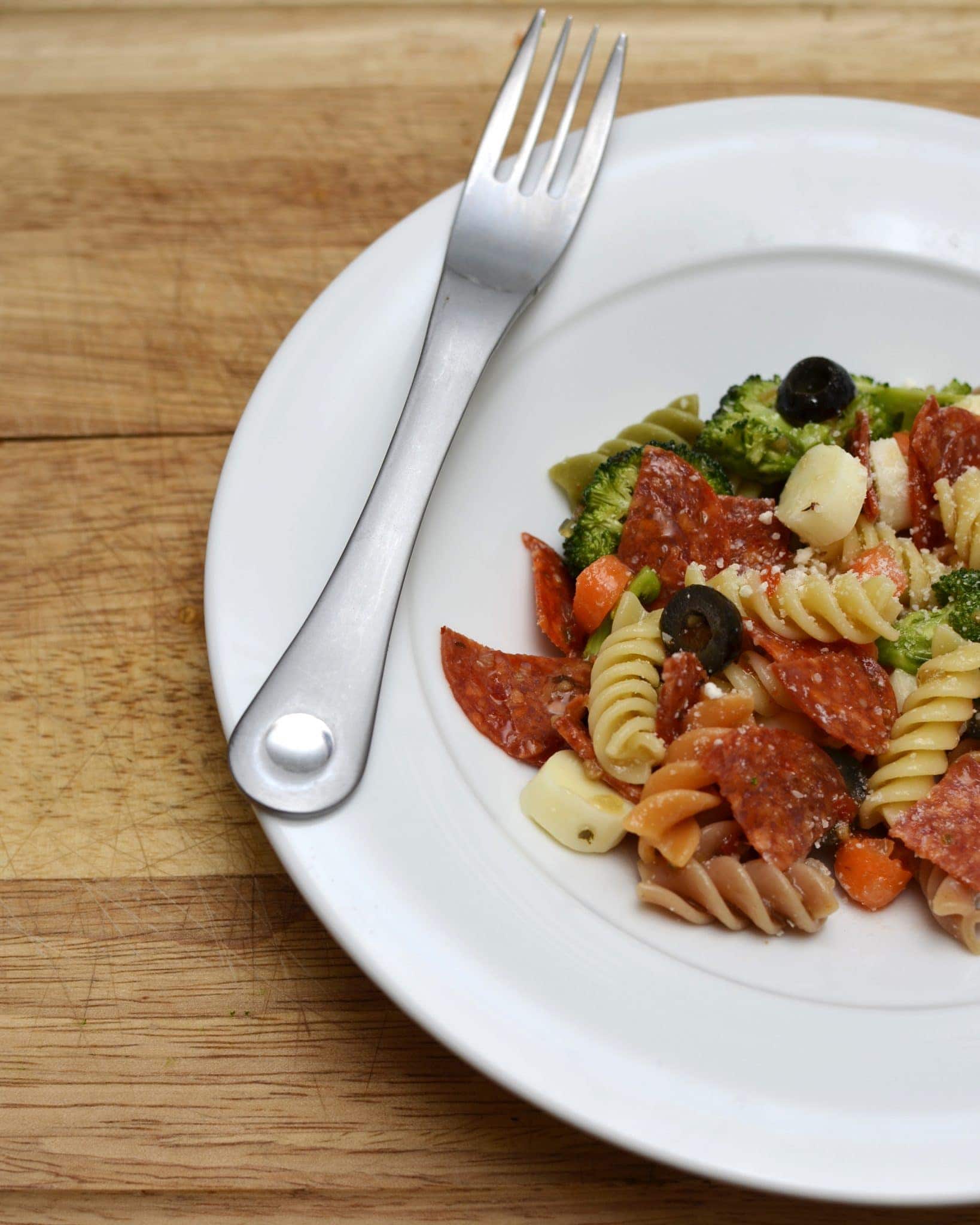Angled view of pasta salad on a white plate with a fork.