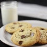 Angled view of chocolate chip cookies on a white plate with milk in the background.
